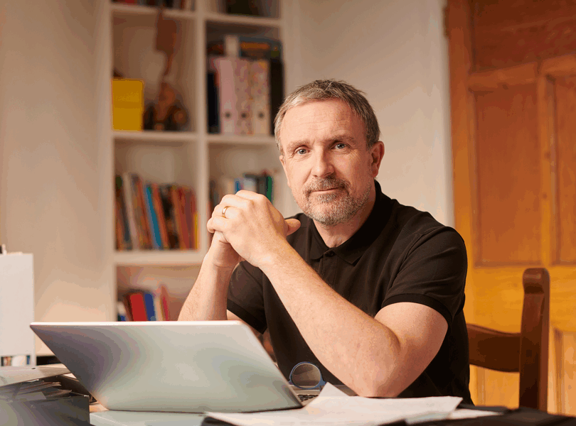 a man who is a landlord, sitting at a table with his laptop open, smiling at the camera